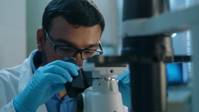 Life scientist working at a laboratory. Young indian male life scientist looking at a blood sample through microscope.
