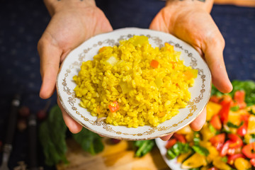 Woman hands holds cooked bulgur porridge pilaf or pilau served with raw vegetables salad. Yellow turmeric meal. Vegan vegetarian healthy food. Traditional Arabic asian food