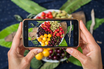 Smartphone photography of food. Woman hands take phone photography of buddha bowl with fruits and...