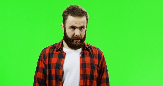 Caucasian man with a beard in the plaid red shirt standing in front of the camera with a face like he is bored and cant stand it no more. Green screen. Chroma key.