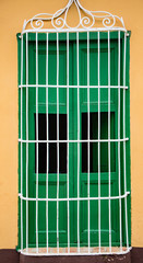 Green shuttered window with white bars on orange wall, newly painted