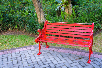 Bright red bench on brick patio in a lush tropical garden
