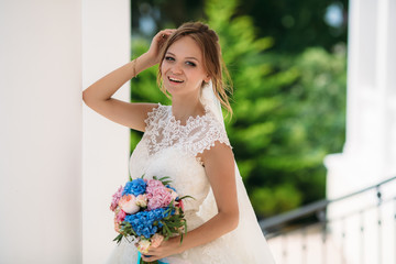 Portrait of a laughing bride in a lace dress and a bouquet of different colors. The girl is standing on the street and the wind is developing her light vaults.