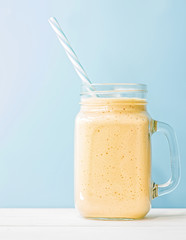 summer drink mango milkshake in mason jar with drinking straw on blue background