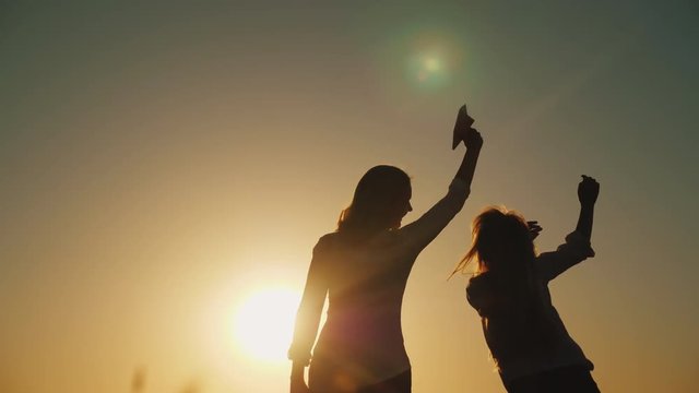 Happy mother with her daughter playing with a paper airplane at sunset