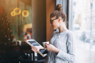 Fototapeta premium Young girl looking at tablet and smiling in cafe with big window.