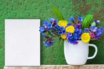 Bouquet of primroses blue lungwort in white enameled metal mug on table and vintage background, grunge with white paper sheet for text, vintage, copy space, mock up
