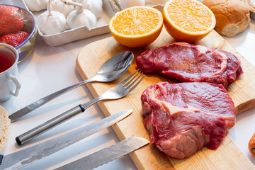 Raw beef with orange and another on wood chopping block with cookware