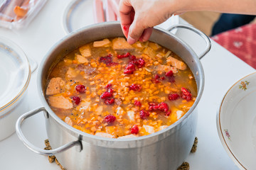Hand pouring raspberry into Salmon soup with carrot and vegetables in stainless pot