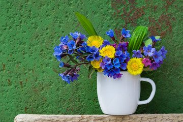 Bouquet of primroses blue lungwort in white enameled metal mug on table and vintage background, grunge with place for text, vintage, copy space
