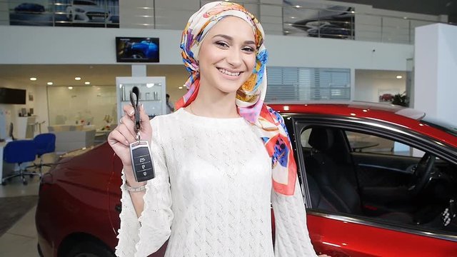 Muslim woman with car key over car show background