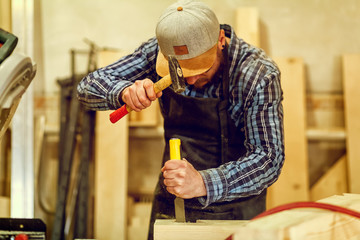 Strong carpenter  in work clothes  carving wood using a woodworking tool, chisel, hands close up, carpentry and craftsmanship concept