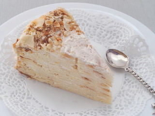 Portion of multi layered cake upon white plate. Puff pastry cake decorated with crumbs. Selective focus.