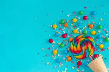 Foto op Plexiglas Ice cream waffle cone with colorful lollipop on stick, scattering of multicolored sweets and confectionery topping. Still life on blue background.Copy space,  Flat lay, Top view,  greeting card © IRINA