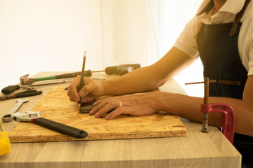 Close-up of male carpenter hands drawing mark on wooden flooring with steel ruler and pencil.