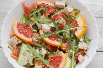 Healthy salad with grapefruit slices, fresh arugula (rocket) leaves, red cherry tomatoes, cucumber and chicken breast in white bowl, top view