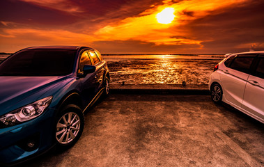 Blue and white compact SUV car with sport and modern design parked on concrete road by the sea at sunset. Environmentally friendly technology. Business success concept. Two cars