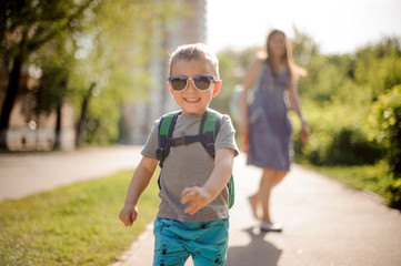 Smiling little boy walking down the street with his mother