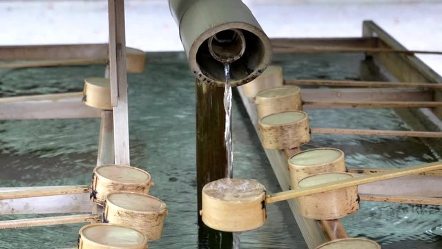 close up of a water fountain and bamboo dippers used for ritual purification at meiji shrine in tokyo, japan