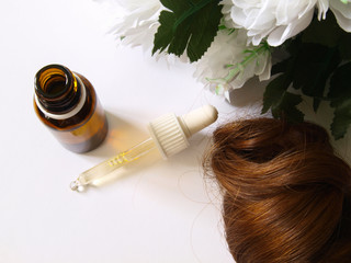 Fototapeta premium Argan oil bottle with a pipette, lock of hair, white flower, from above.