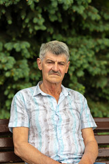 Fototapeta premium An ELDERLY MAN sitting on a background of green trees