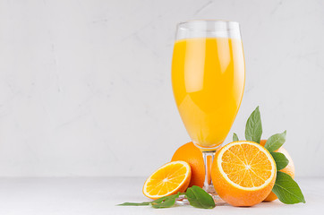 Healthy homemade lemonade - orange juice in wineglass with oranges and green leaves on white wood background.