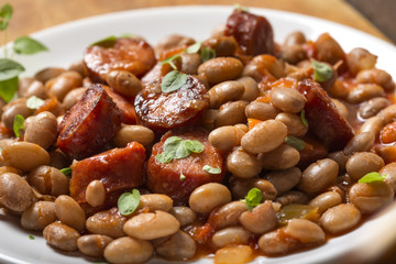 Beans with smoked pork sausages on plate and tomato sauce with green herbs