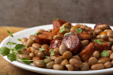 Beans with smoked pork sausages on plate and tomato sauce with green herbs