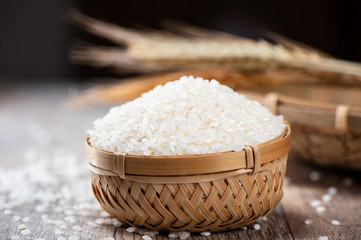 raw rice in a bamboo basket with wheat on wooden background