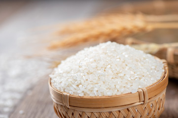 raw rice in a bamboo basket with wheat on wooden background
