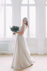 Fototapeta premium Beautiful bride in a wedding dress in a bright stylish Studio. Wedding in European style. Decor and bouquet in hand. Young girl standing, sitting and posing