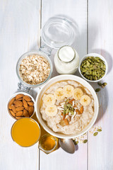 bowl of oatmeal with banana, honey and nuts on white background, vertical top view