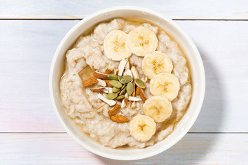 bowl of oatmeal with banana, honey and nuts on white table, top view