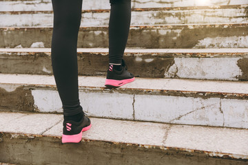 Fototapeta na wymiar Cropped photo close up of female legs in sportswear, black and pink woman sneakers doing sport exercises, climbing on stairs outdoors. Fitness, healthy lifestyle concept. Copy space for advertisement.
