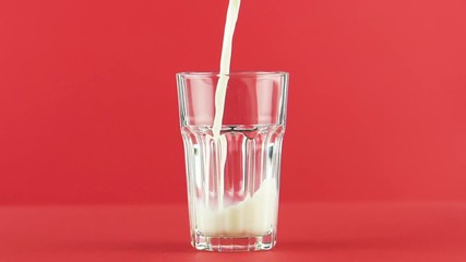 Slow motion close-up shot of cold diary milk cold beverage drink pooring into faceted glass on colored red background in studio