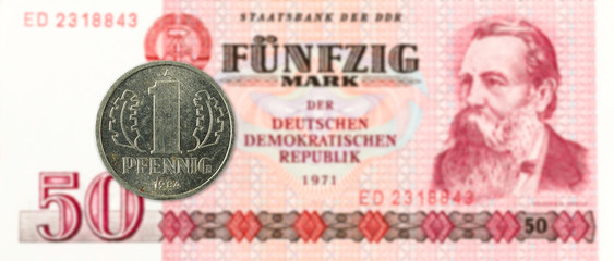 1 pfennig coin against historic 50 east german mark bank note
