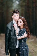 Fototapeta premium Young stylish couple in the forest, running around the Park and laughing. Modern people on a walk. Beautiful girl with tattoos. Loving young man and girl. mountain Park with pine forest