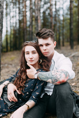 Young stylish couple in the forest, running around the Park and laughing. Modern people on a walk. Beautiful girl with tattoos. Loving young man and girl. mountain Park with pine forest