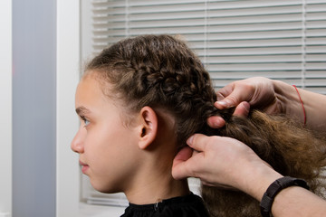 the hairdresser plaits a pigtail to a child, with curly hair