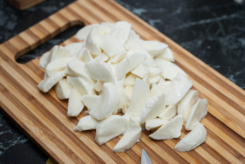Fototapeta na wymiar Chopped fresh mozzarella cheese with kitchen knife on wooden cutting board. food preparation Process.