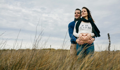 Pregnant making a heart with hands on her naked belly while her partner embraces her