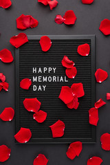Black letterboard with white plastic letters with quote Happy Memorial Day, and rose petals on black background.