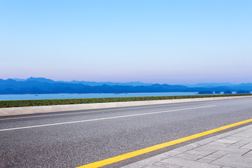 asphalt road and blue sky with white clouds by the lake