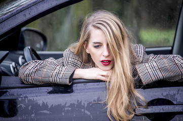 Lovely young blonde woman is leaning out of the window of her car. Lifestyle concept.