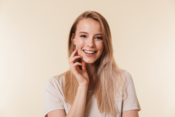 Fototapeta premium Portrait of gorgeous woman 20s with european appearance in basic t-shirt smiling at camera, isolated over beige background in studio