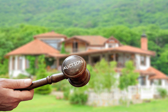 Concept real estate auction,blurred house background and wooden gavel in a hand