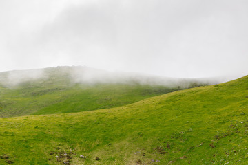 Beautiful mountain landscape with green hills on a cold foggy day, with sky and clouds