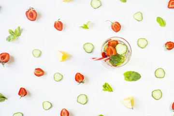 A glass of water with the addition of strawberries, cucumber, mint and lemon. Among the bright ingredients on a white background. Detox and Sports Concept. Top view, flat lay