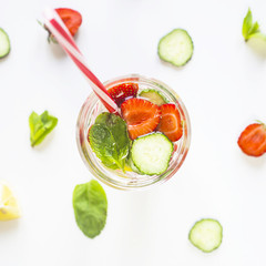 A glass of water with the addition of strawberries, cucumber, mint and lemon. Among the bright ingredients on a white background. Detox and Sports Concept. Top view, flat lay