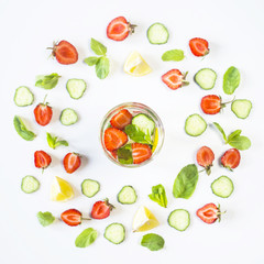 A glass of water with the addition of strawberries, cucumber, mint and lemon. In a circle of bright ingredients on a white background. Detox and Sports Concept. Top view, flat lay